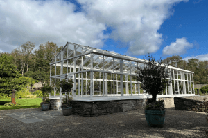 The exterior of the glasshouse at Vandeleur Walled Garden & Visitor Centre. Glasshouse surrounded by potted plants and blue skies.