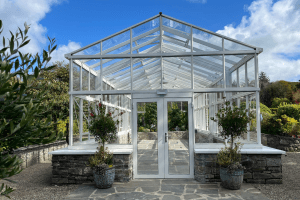 The front facing exterior of the glasshouse at Vandeleur Walled Garden & Visitor Centre. Glasshouse surrounded by potted plants and blue skies.