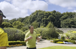 An image of the head gardener giving a guided tour of the walled garden to a tourist in a peaked cap.