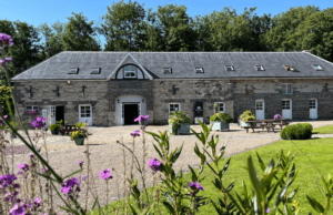 Image of the lower building at Vandeleur Walled Garden. The Woodlands room is on the ground floor. The image shows the exterior of the building on a sunny day with purple flowers in the foreground.
